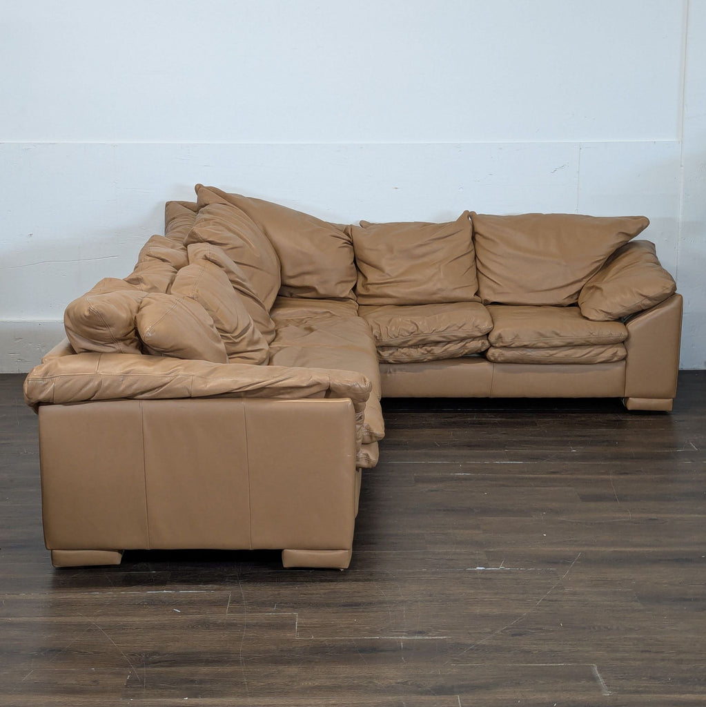 2. L-shaped tan leather sectional with soft, overstuffed cushions, set against a simple white wall.