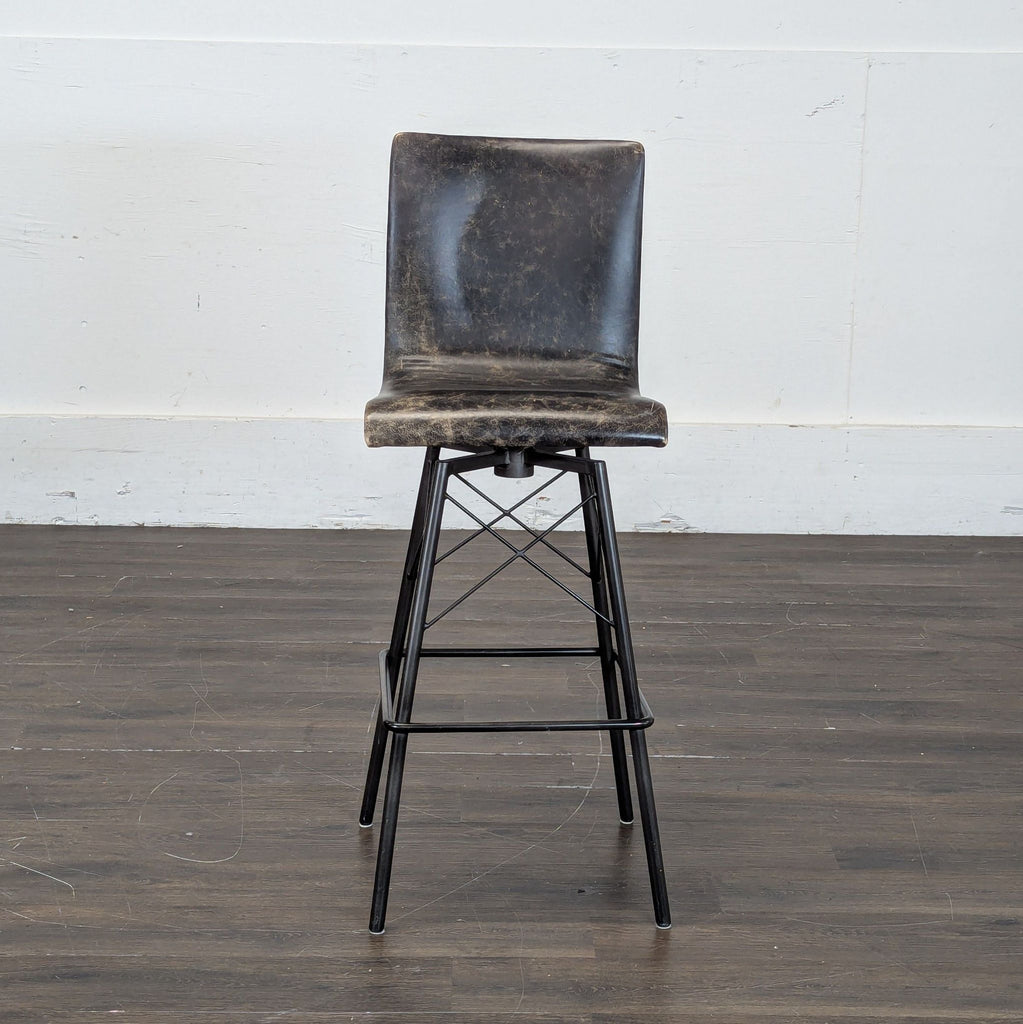 3. Single Four Hands counter stool in worn black leather finish and angled metal legs, shown against a plain wall.