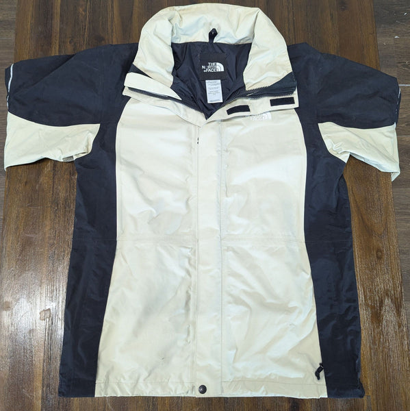 1. The North Face men's jacket in beige and black, shown laid flat on a wooden surface with short sleeves.
