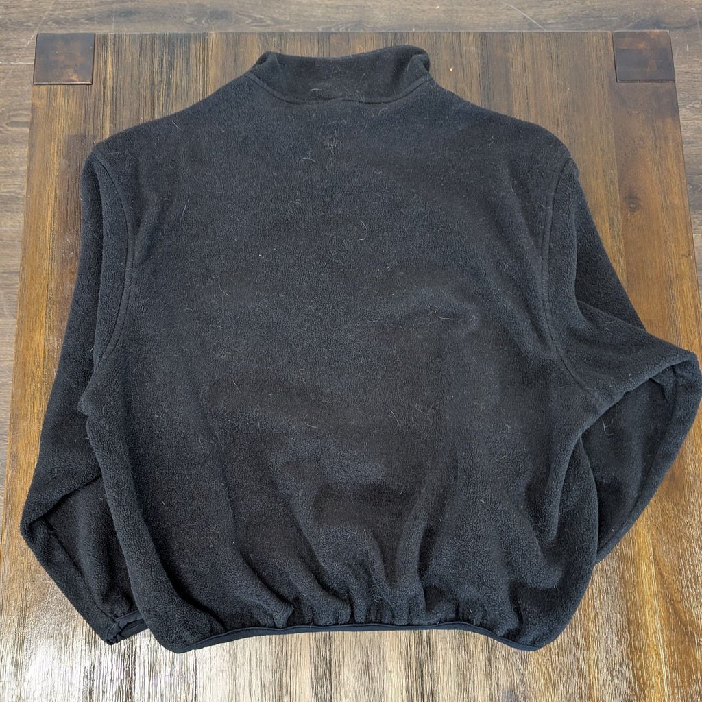 2. Back view of a black men's Woolrich fleece pullover with elastic hem, displayed on a wooden surface.