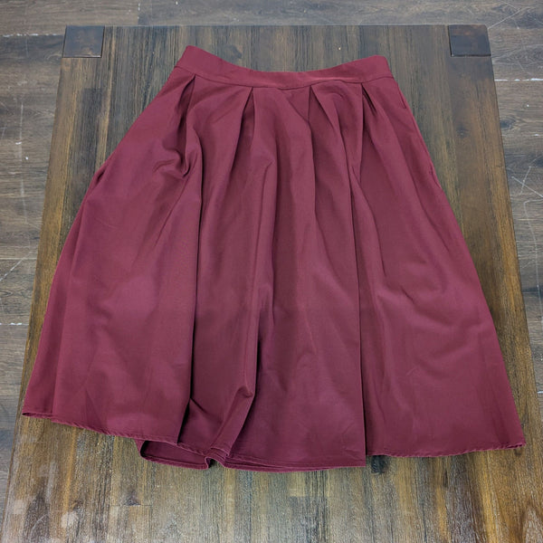 1. A burgundy pleated midi skirt for women from Urban Coco, displayed flat on a wooden surface.