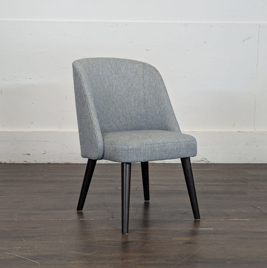 3. Angled side view of a Room & Board upholstered gray dining chair with tapered dark wooden legs.