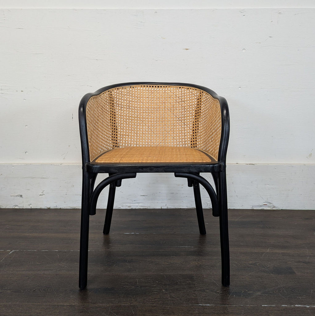 3. Wooden dining chair with black legs and a curved cane backrest and seat, placed on a wood floor indoors.