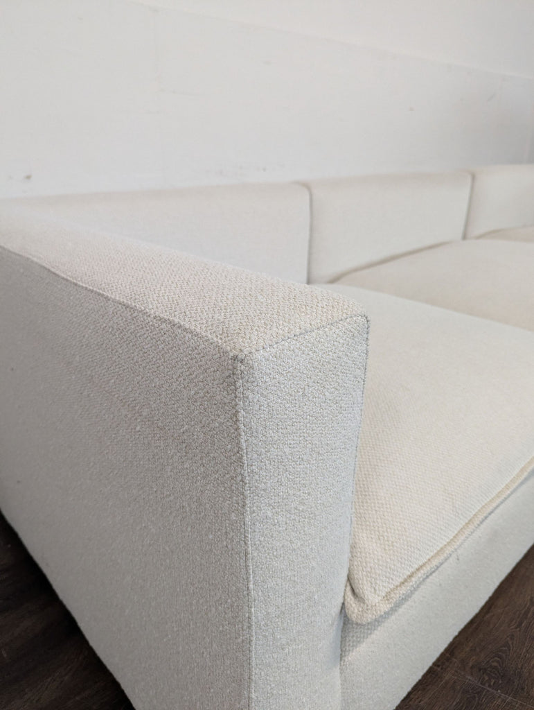 1. Close-up of a Crate & Barrel 3-seat sofa arm and cushion in light beige fabric, set against a white wall.