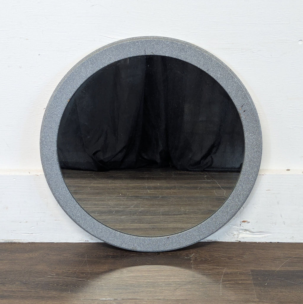 3. Round mirror with a textured grey frame, placed on a dark wood floor against a white wall.