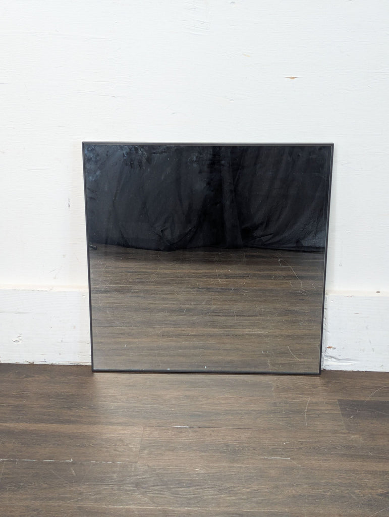 2. Minimalist Pottery Barn mirror with black frame leaning against a white wall on a dark wooden floor.