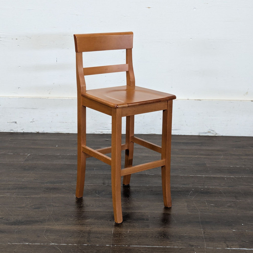 2. Angled view of a light wood counter stool featuring a flat seat and ladder-style backrest.