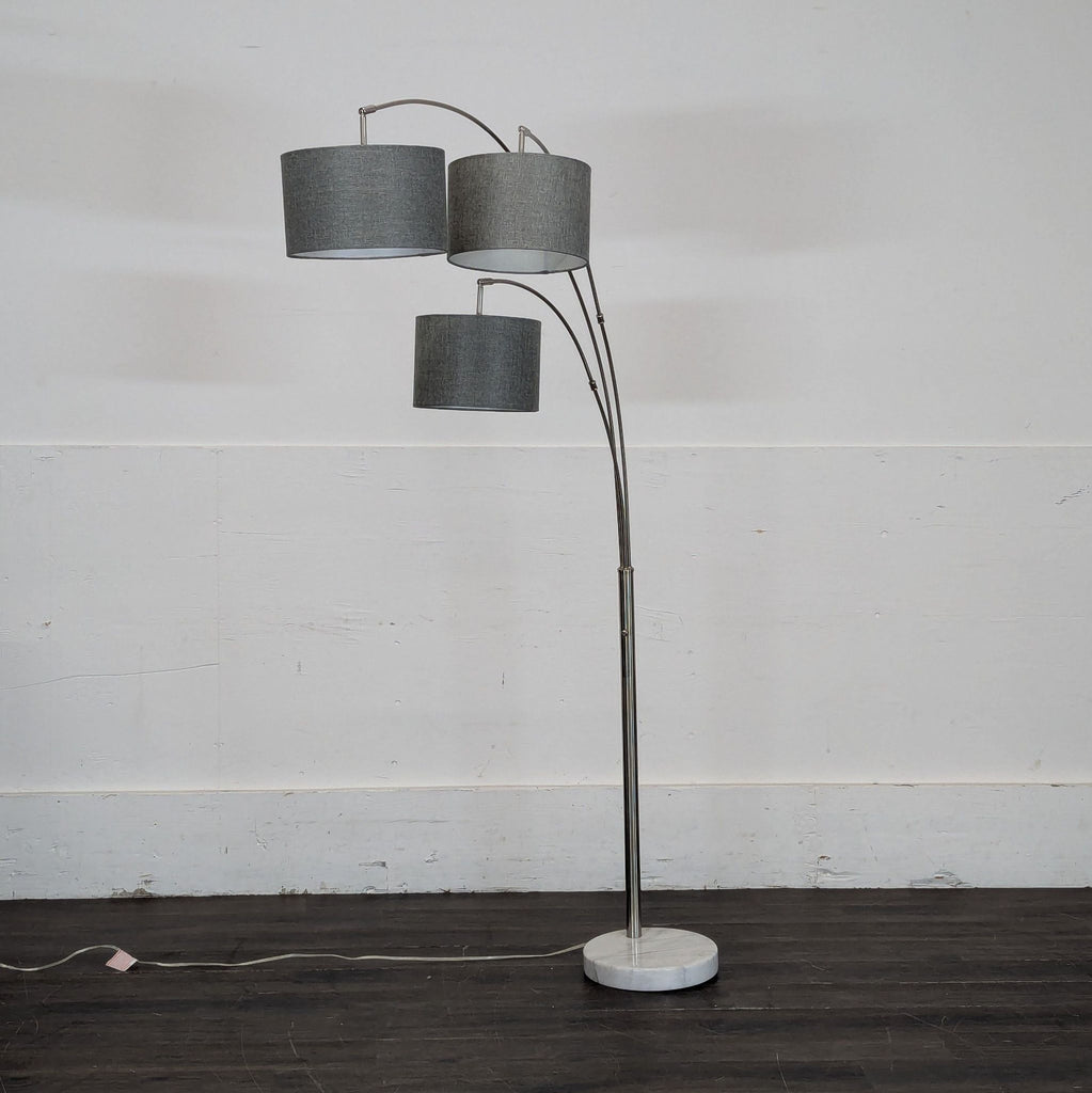1. Modern floor lamp with three curved arms and grey drum shades on a marble base, standing against a wall.