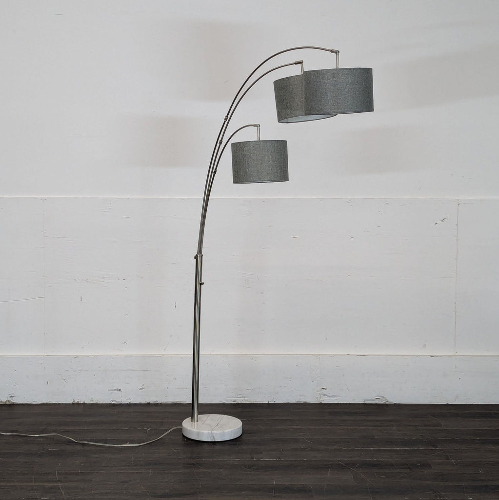 2. Side view of a contemporary arched floor lamp with grey fabric shades and a round marble base on a dark floor.