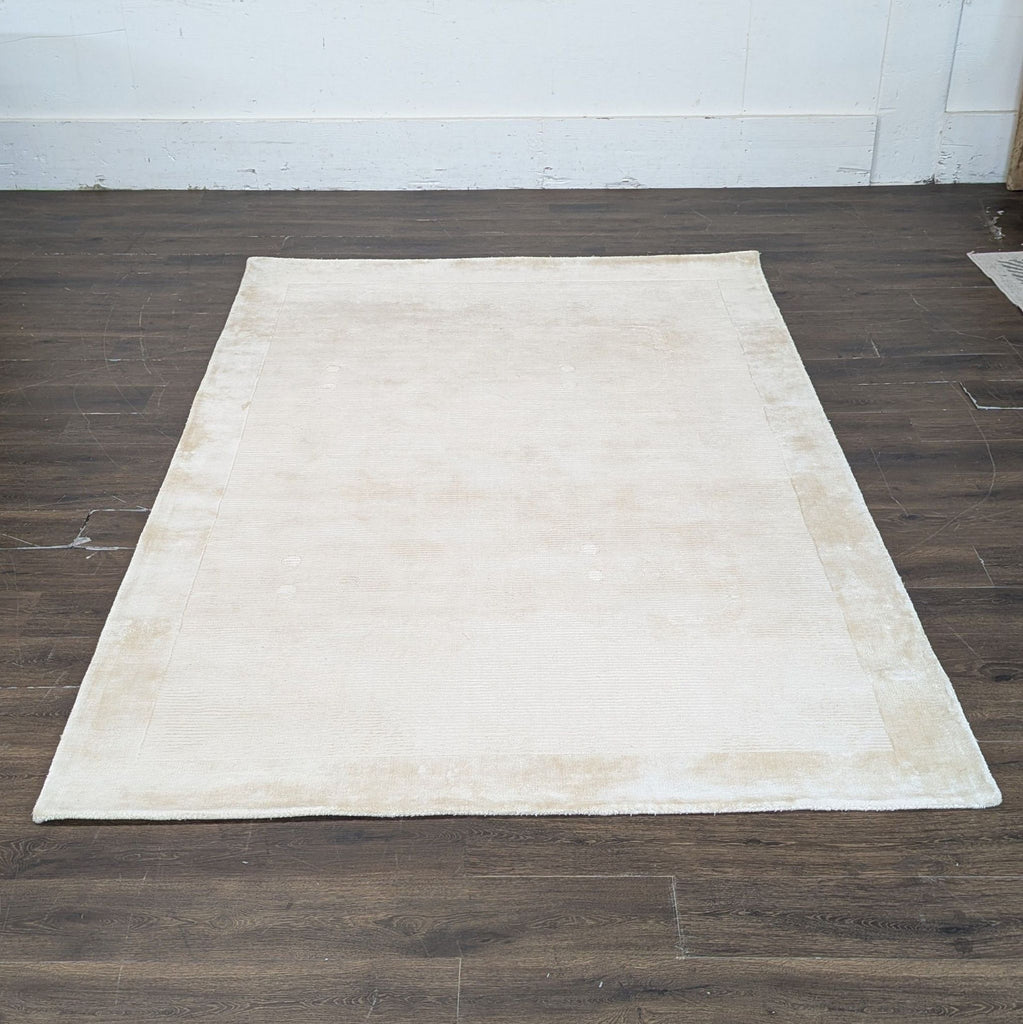 2. Large rectangular beige West Elm rug with a subtle border, shown on a dark wood floor.  