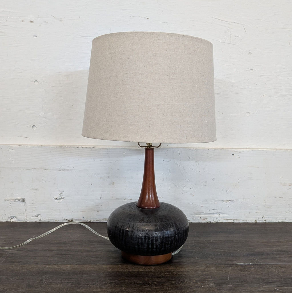3. Contemporary lamp with neutral fabric shade, slim wooden stem, and textured black base on wood floor.
