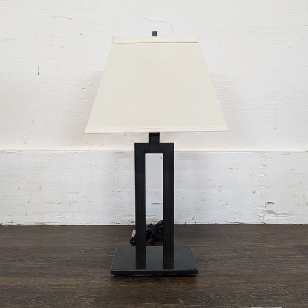 1. Modern table lamp with a black geometric metal base and white square lampshade, seen against a white wall.