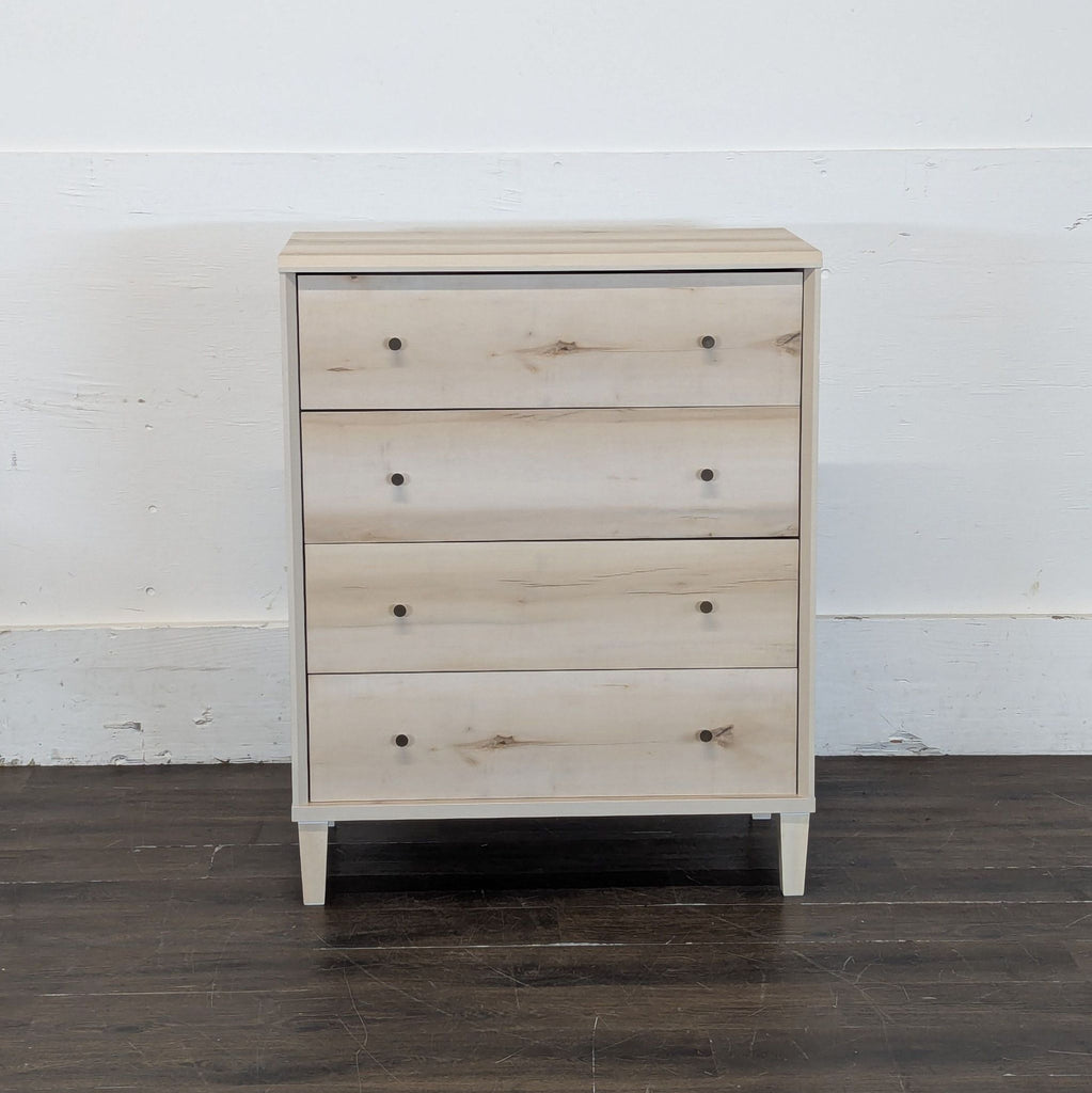 3. Modern light wood dresser with three spacious drawers and dark knobs, set on a hardwood floor.