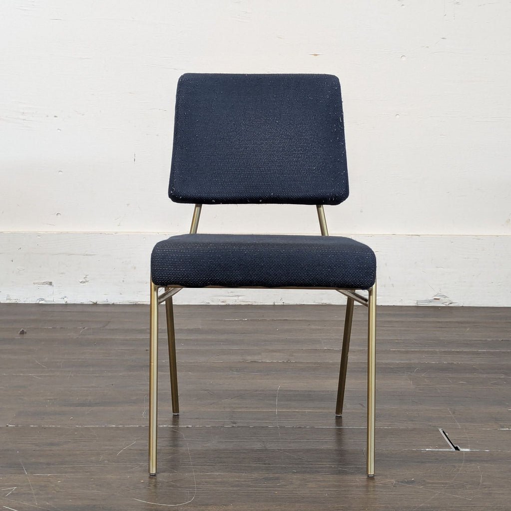 2. Single West Elm dining chair featuring navy fabric and slim gold legs against a plain white wall and dark floor.  
