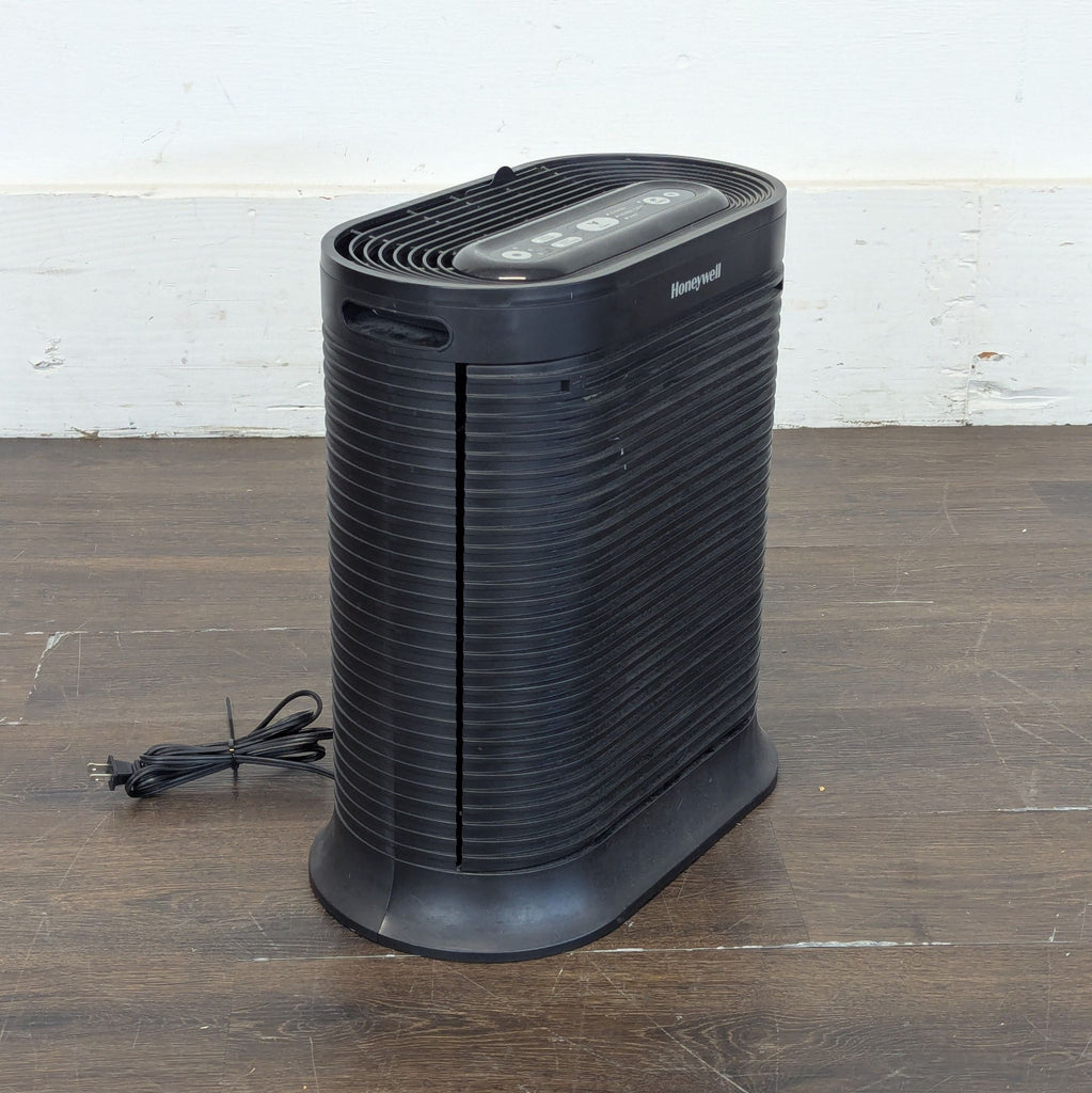 2. Angled side view of a Honeywell black AC & Fans appliance with power cord, on a wooden floor.