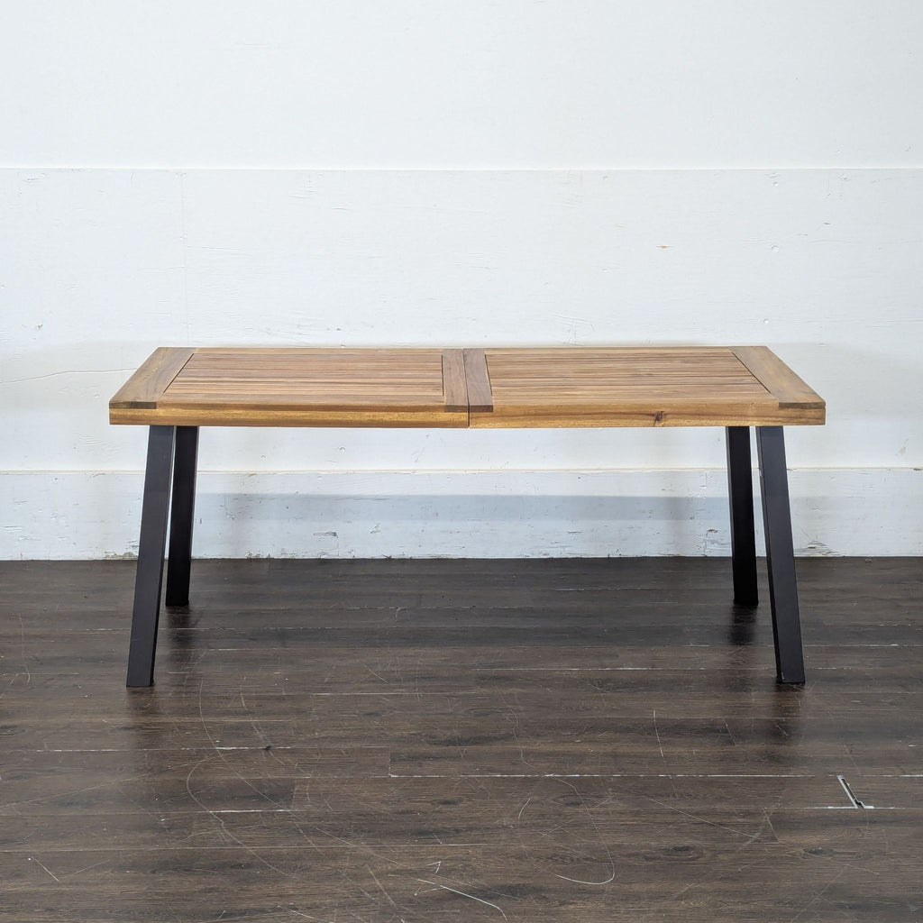 1. Rectangular wooden dining table with black angled legs on a dark floor, viewed from the front.