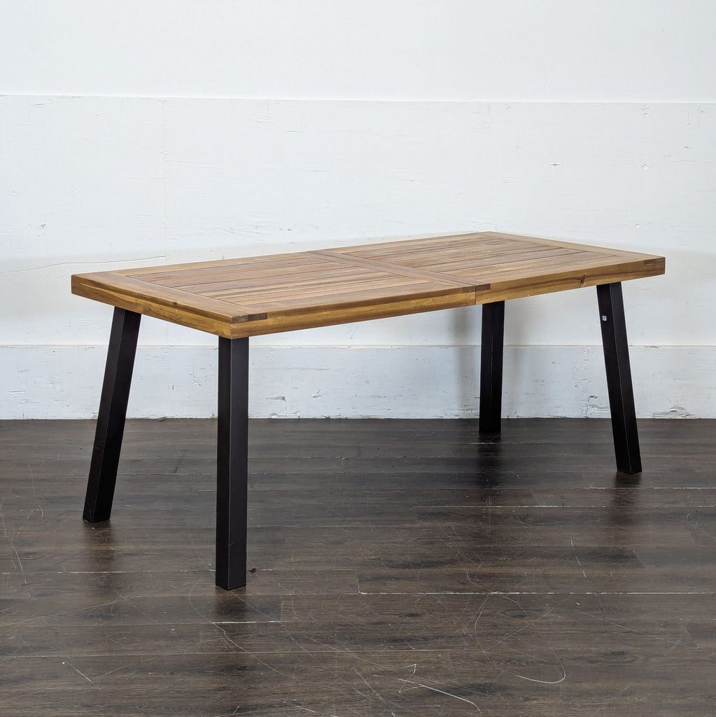 2. Side angle of a wooden dining table with black metal legs, placed on a dark wood floor.