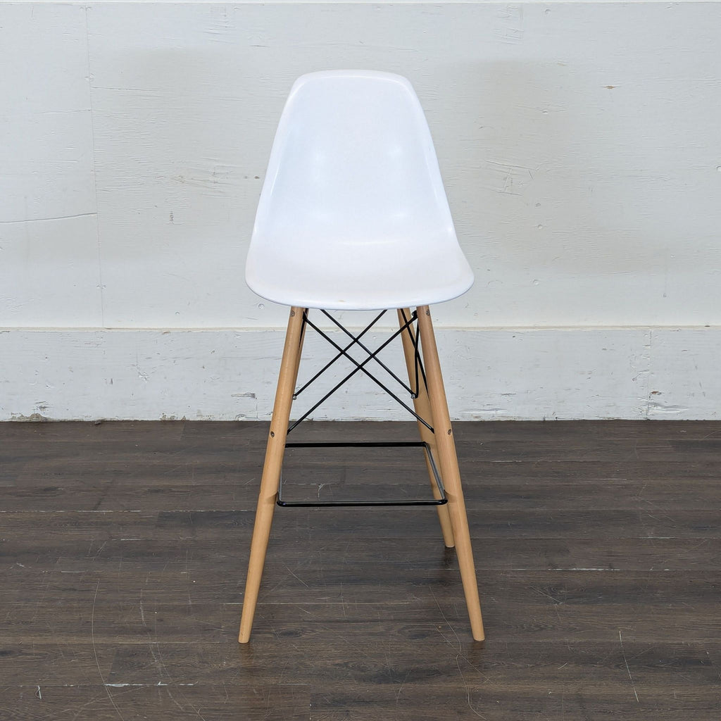 - White dining chair with wooden legs and metal supports, set against a plain wall on a dark floor.