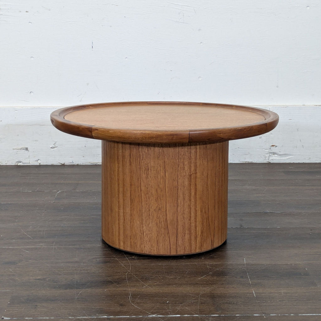 Safavieh coffee table with a circular top and cylindrical base, placed on a wooden floor.