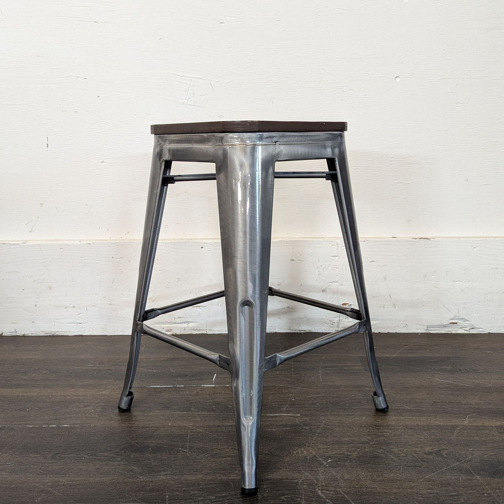 2. Industrial-style metal stool with a square wooden seat and angled metal legs on a dark floor.