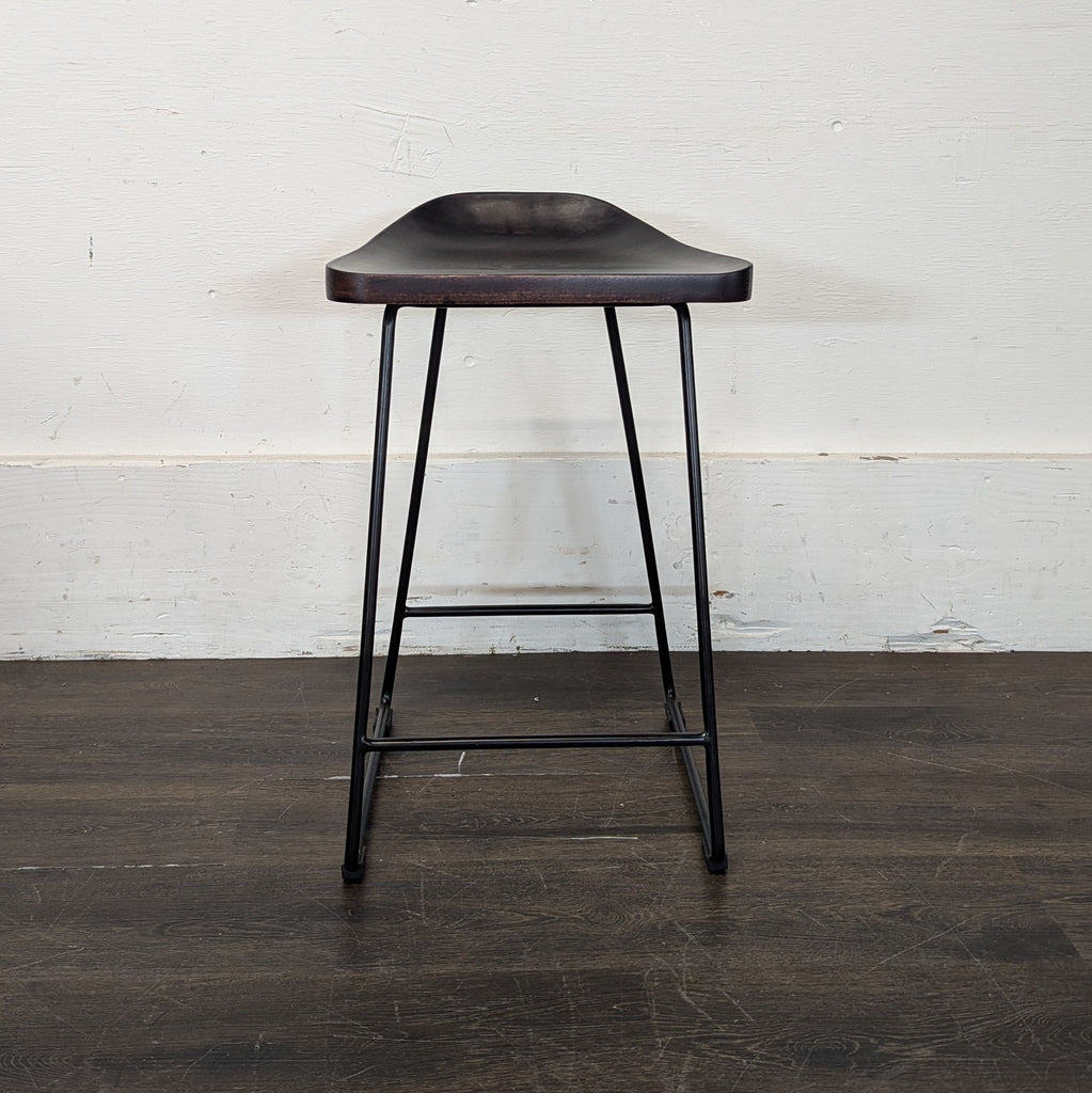 2. Minimalist black Pottery Barn stool with a molded seat and sturdy metal frame, viewed from the front.