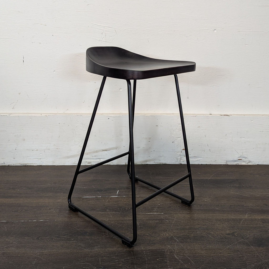 3. Contemporary Pottery Barn stool featuring a curved dark seat and slim metal legs, seen at an angle.