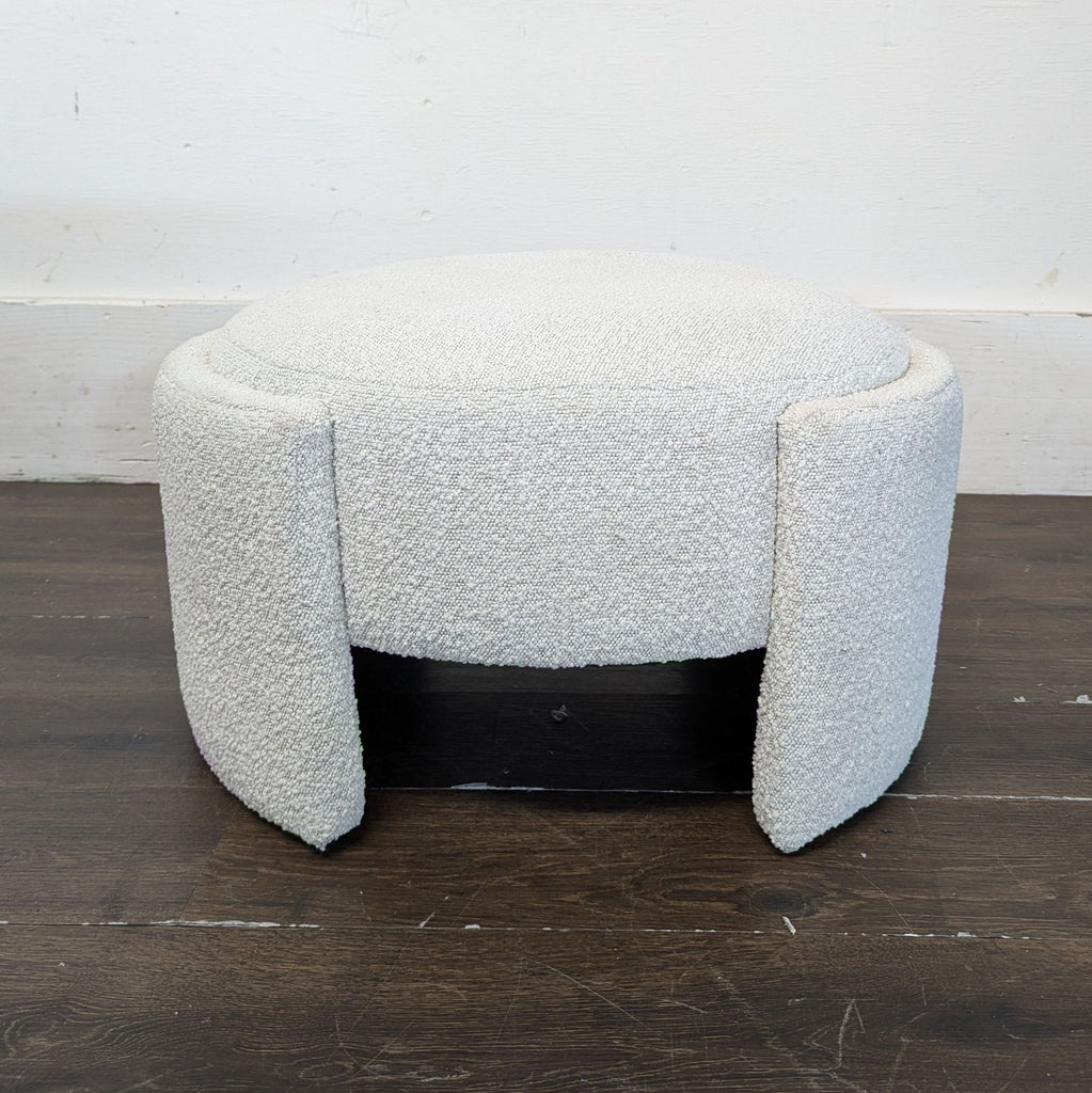 A modern, round white ottoman with three curved legs, textured upholstery, by New Pacific Direct.