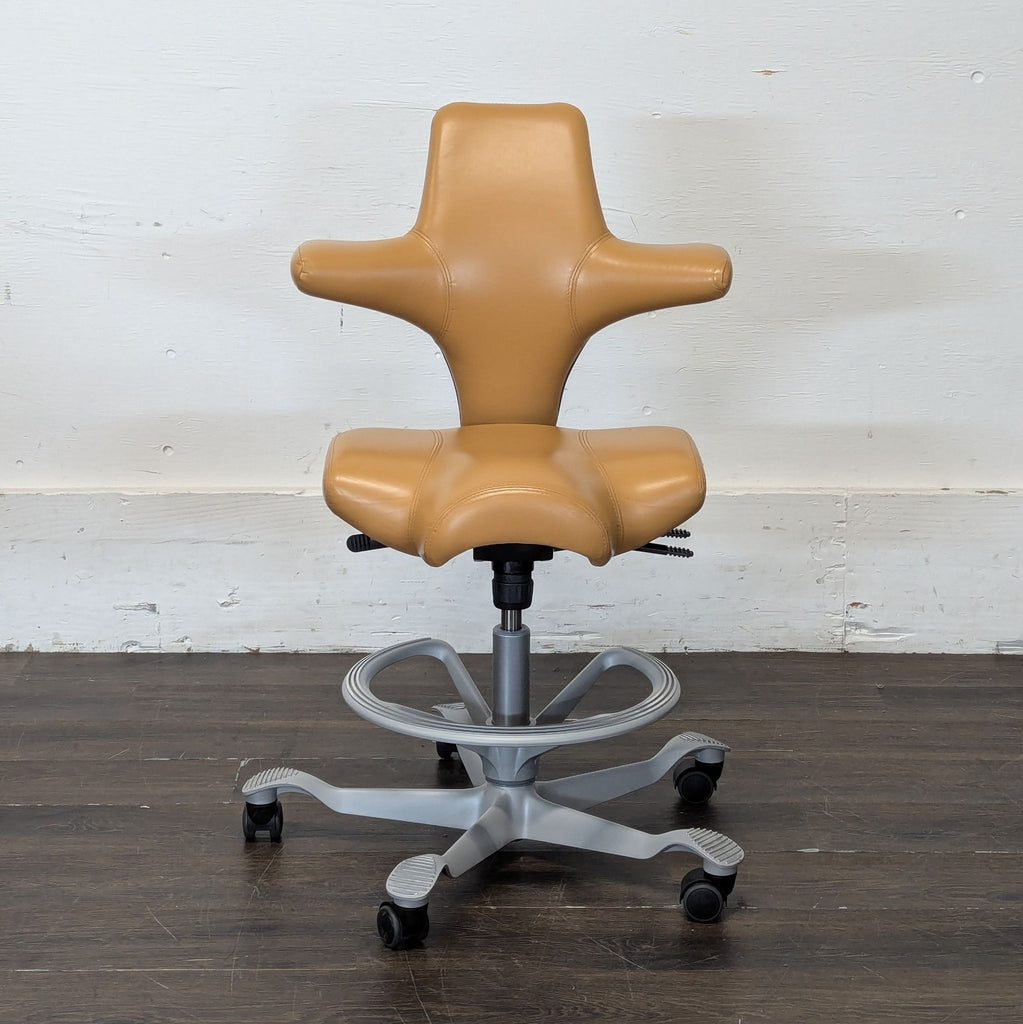 2. HÅG ergonomic tan chair with winged backrest and saddle seat, on wheels and metal base, against wall.
