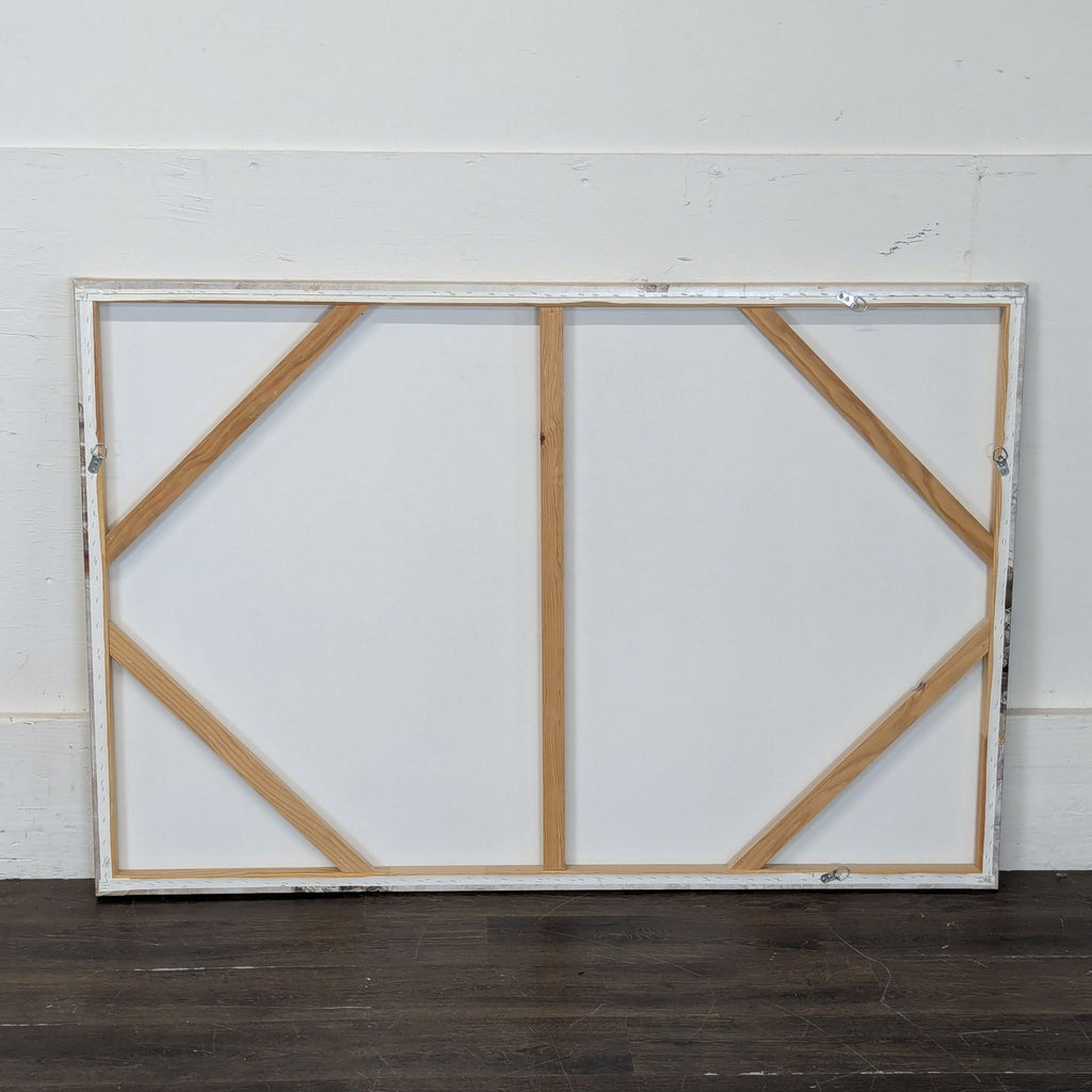 3. Back of a stretched canvas painting, showing wooden support bars and blank canvas resting on a dark wood floor.