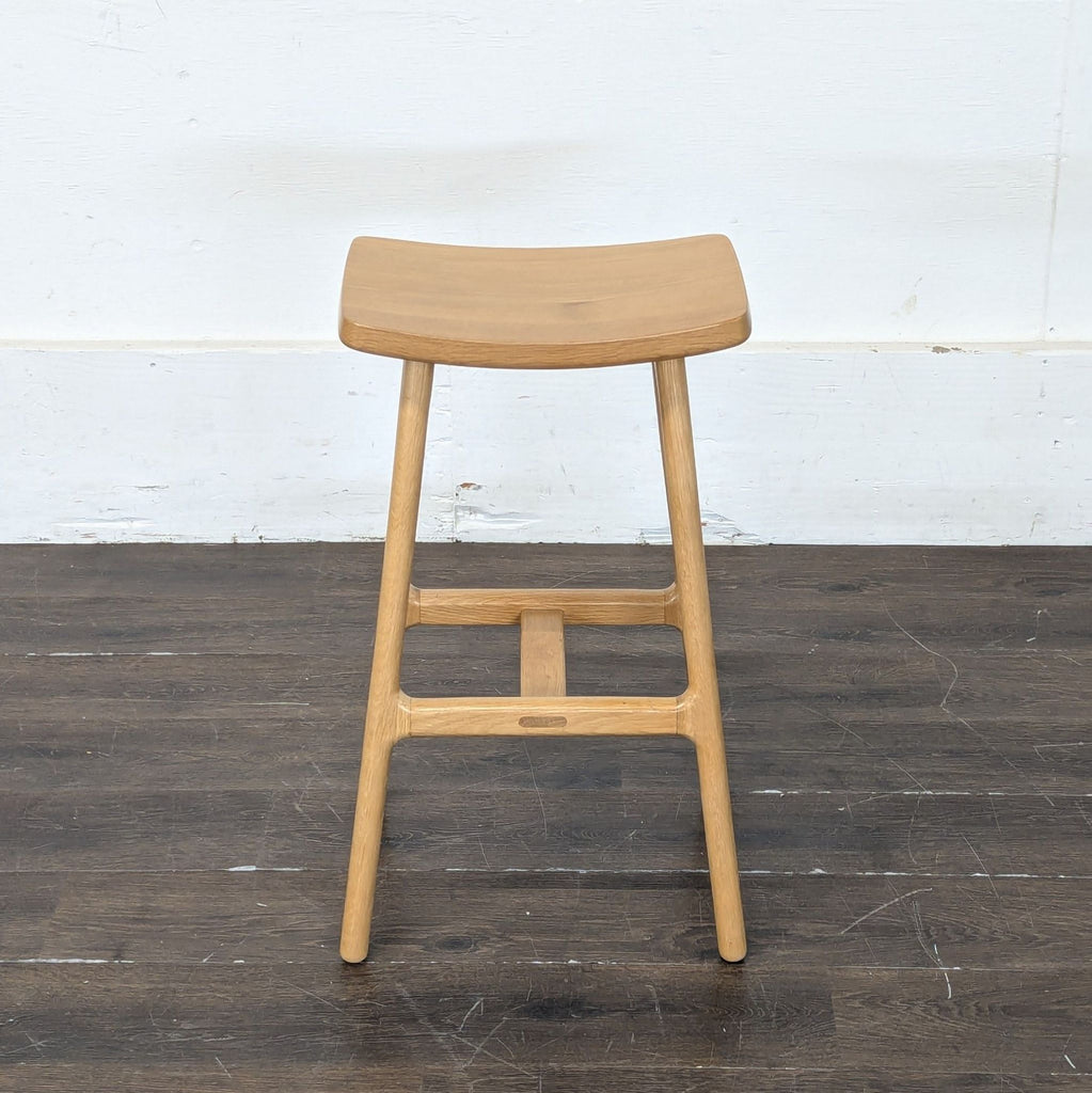 3. Single Article stool with a light wood finish, curved seat, and simple sturdy frame, on wood floor.