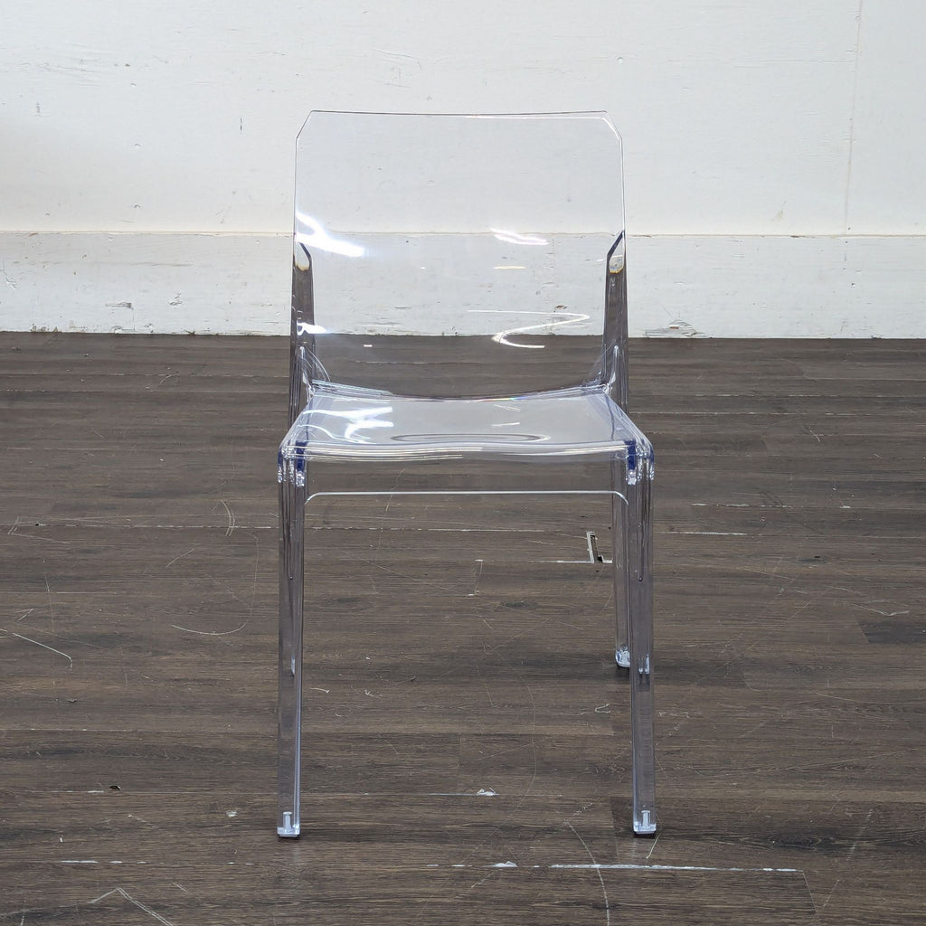 2. Transparent CB2 dining chair with angular backrest, displayed on a dark wood floor against a plain wall.