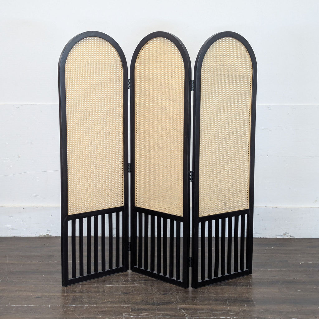 2. Crate & Barrel three-panel screen with arched tops, black wooden frame, and woven cane inserts on wood flooring.