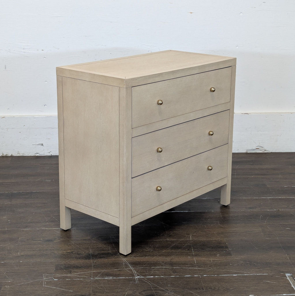 3. Angled view of Butler Specialty Company dresser with light wood finish, three drawers, and gold knobs on a dark floor.