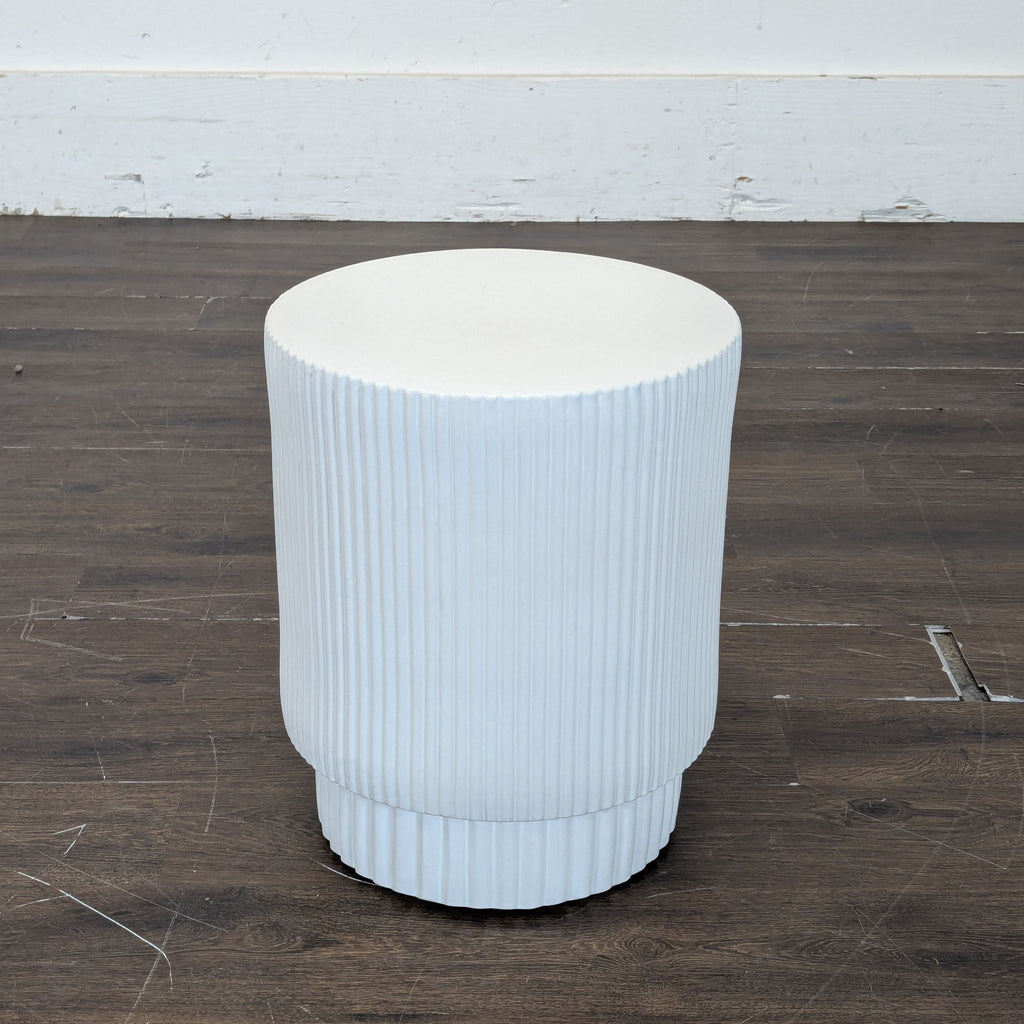 3. Modern white West Elm end table, cylindrical with vertical grooves, displayed on a wood floor background.