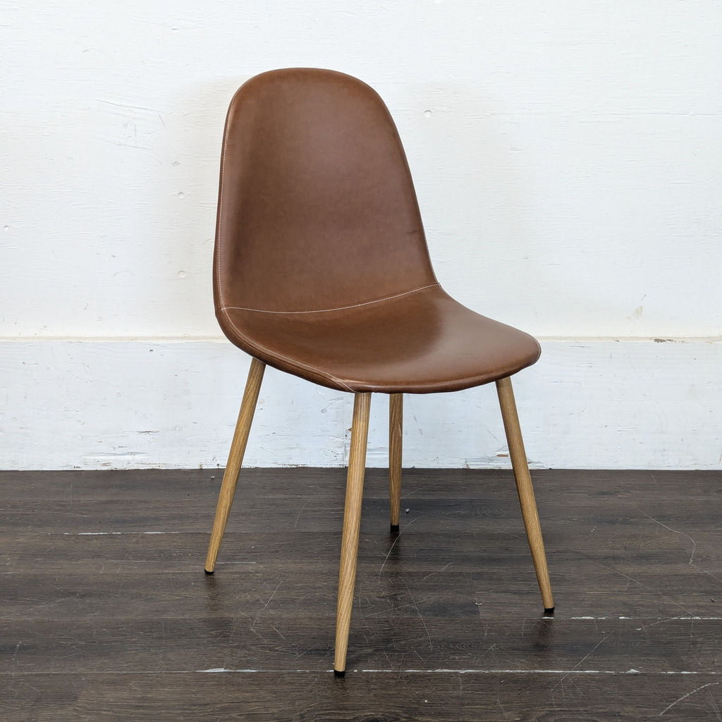 Angled view of a brown dining chair with wooden legs and a smooth, curved backrest on a wooden floor.