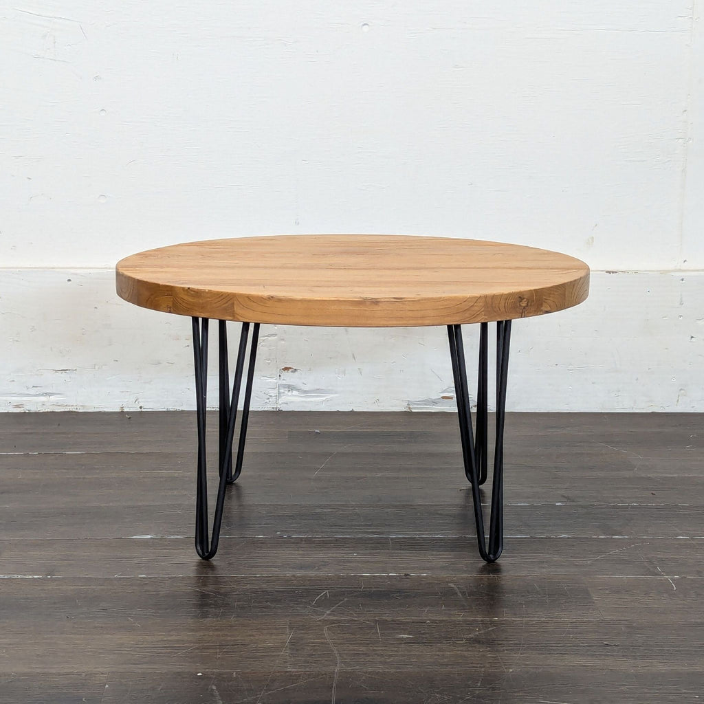 2. Minimalist round coffee table with a wooden top and black hairpin metal legs, displayed on dark wood flooring.