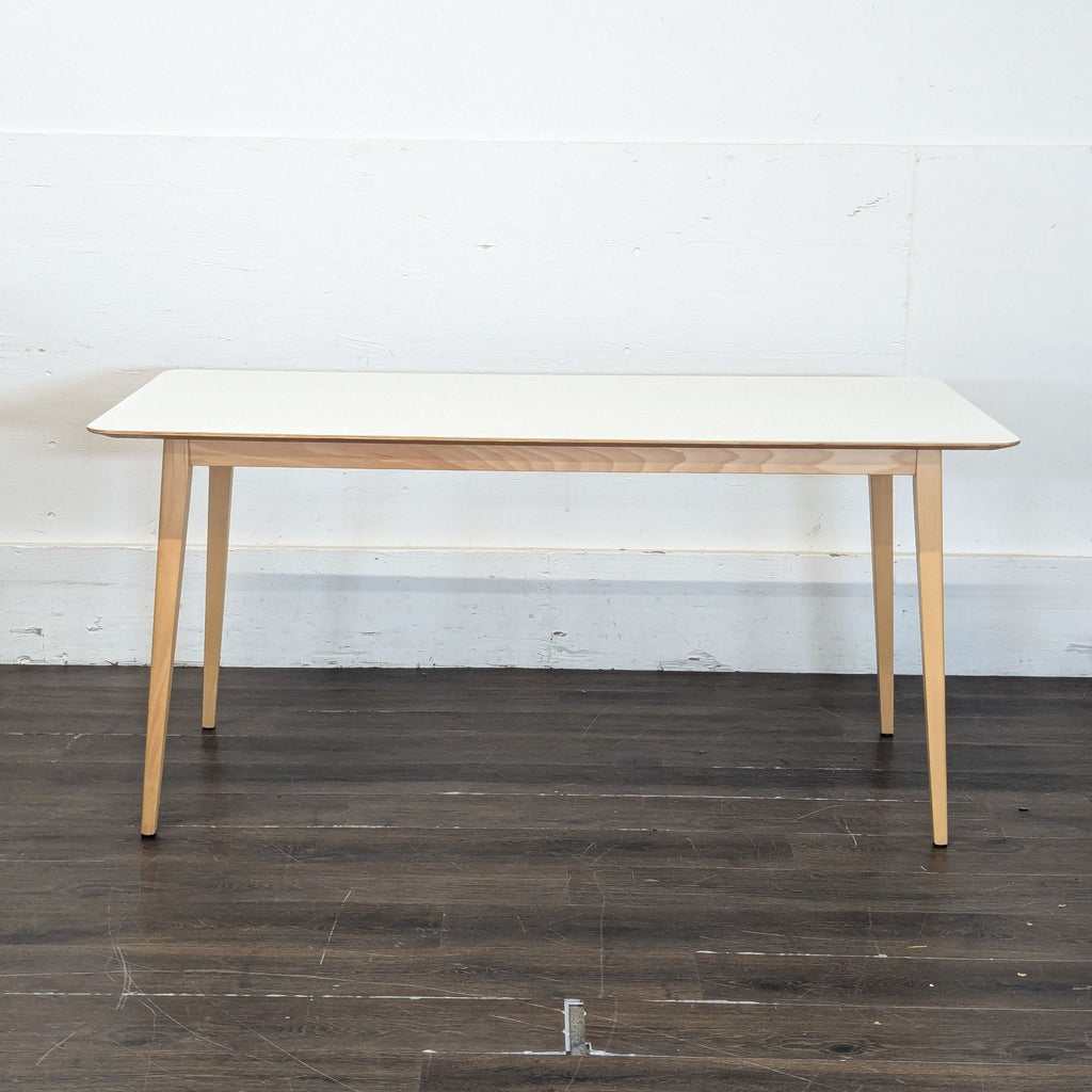 3. Minimalist rectangular dining table with a white surface and natural wood legs, placed against a plain wall.