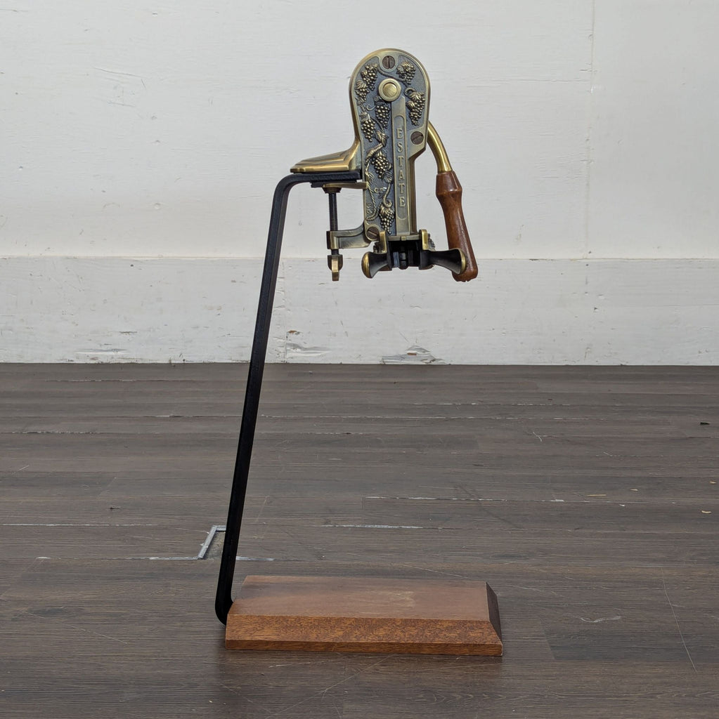 A Rogar Estate vintage-style bottle opener with metal, brass, and wood parts, displayed on a flat wooden platform.