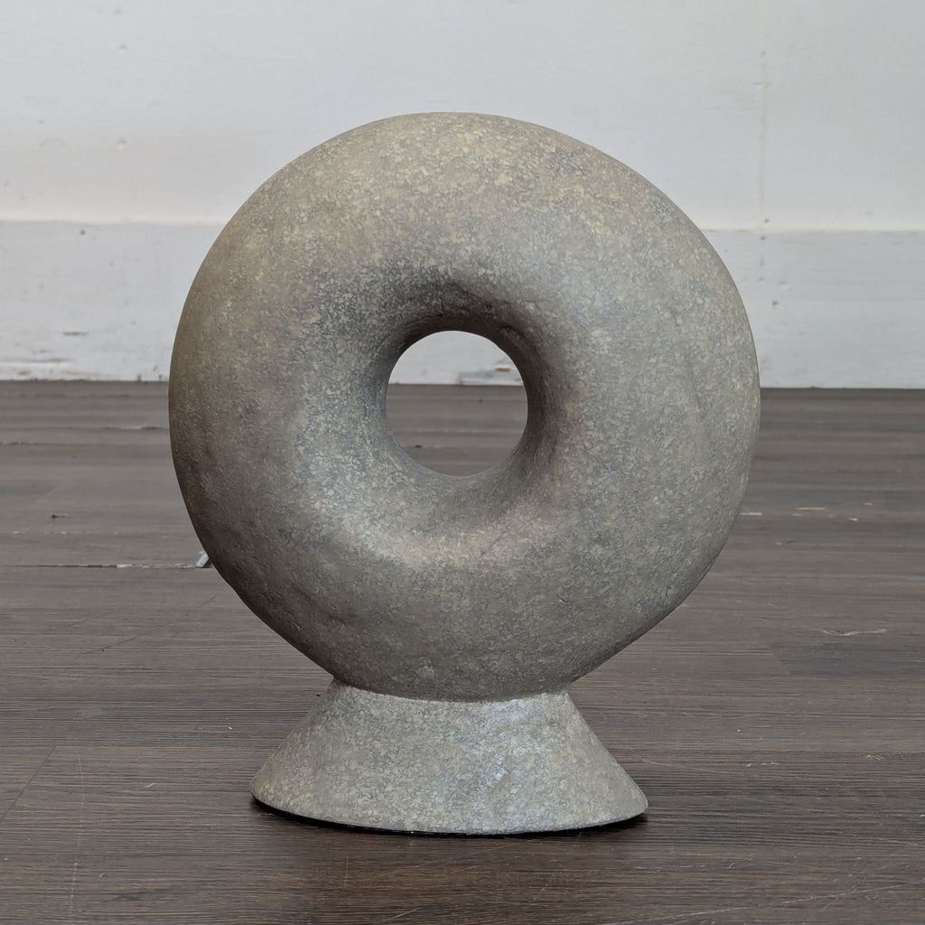 Round stone sculpture with a central hole, donut-shaped, on a small base. West Elm, Sculpture category.  