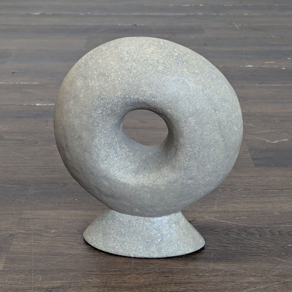 Abstract gray circular stone sculpture with a hole in the center, standing on a conical base. West Elm.