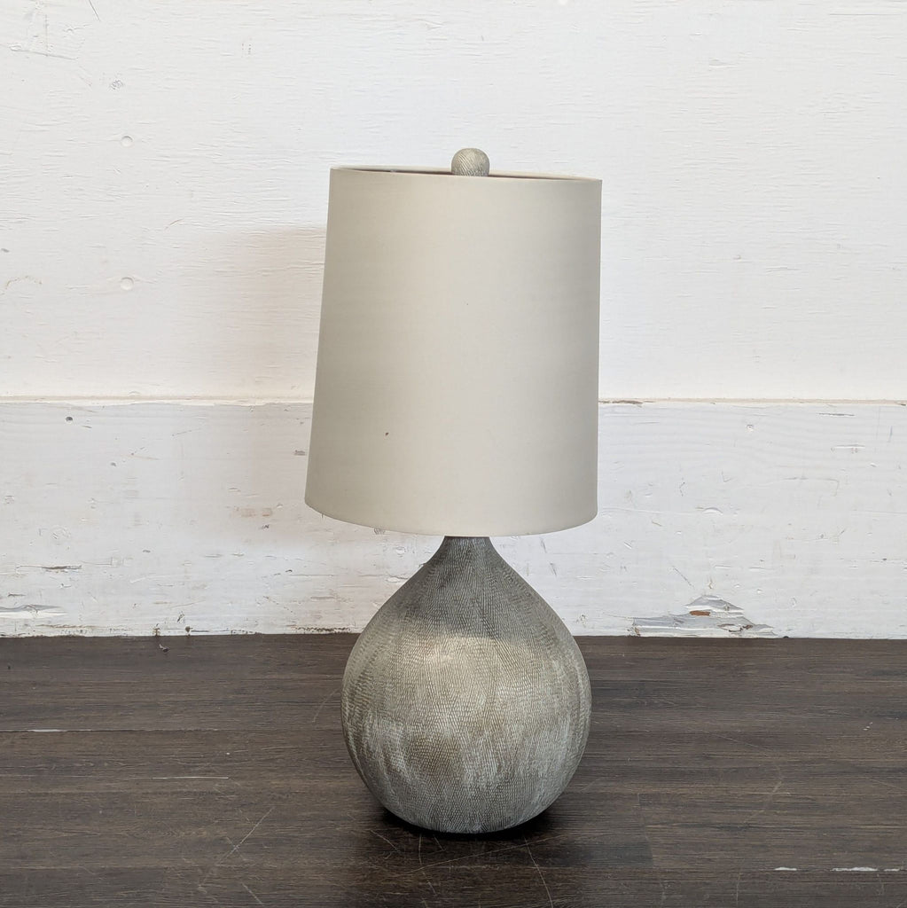 2. Modern lamp with a rounded grey base and a tall, cylindrical cream shade on a dark wood floor.