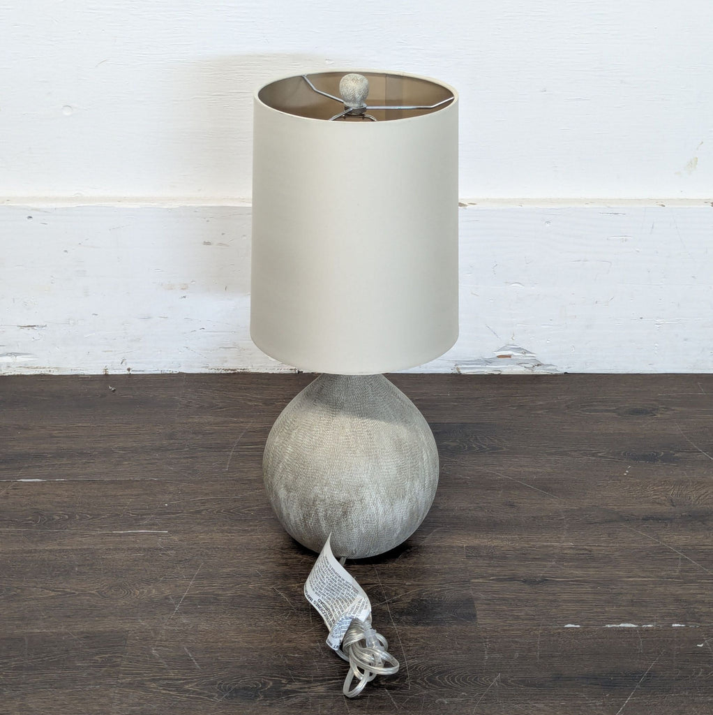 3. Table lamp featuring a grey rounded base, cream shade, and visible wrapped power cord on a wood surface.