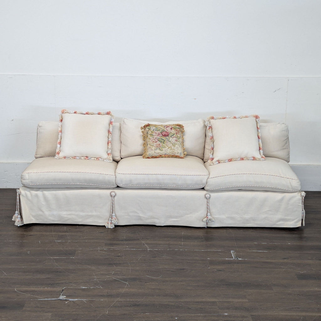2. Elegant cream 3-seat sofa featuring tassel details and three decorative pillows in a minimalist room.