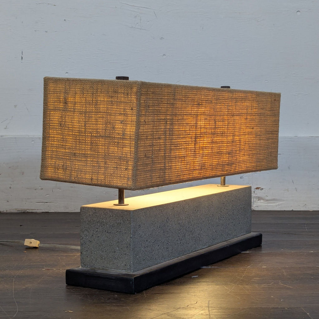 3. Contemporary lighting piece with a boxy tan shade and block concrete base, by Crate and Barrel, side angle view.