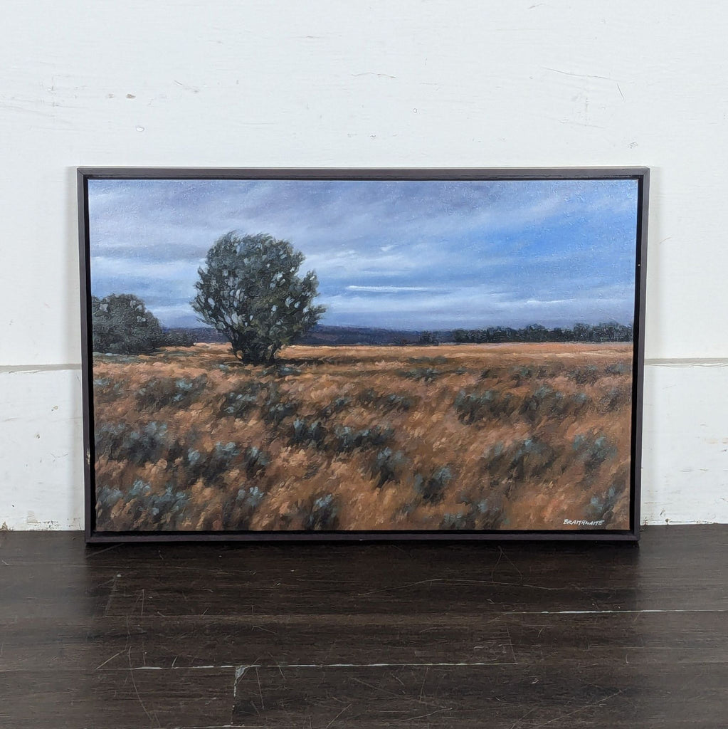 2. Landscape painting of a lone tree in a grassy field with cloudy blue sky, placed against a white wall.