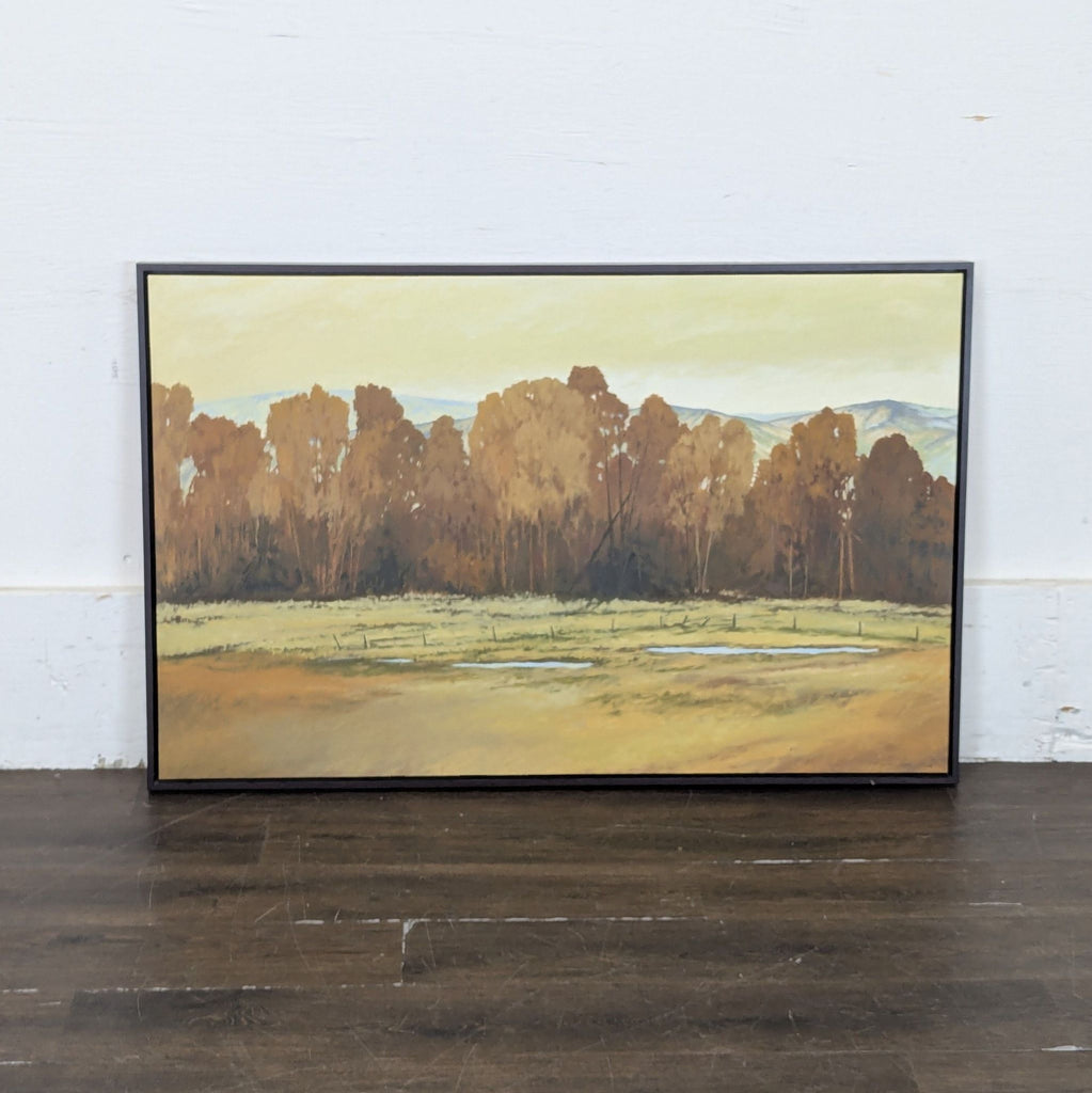 2. Framed painting of brown and gold trees, grassy foreground, and faint hills, displayed against a white wall.