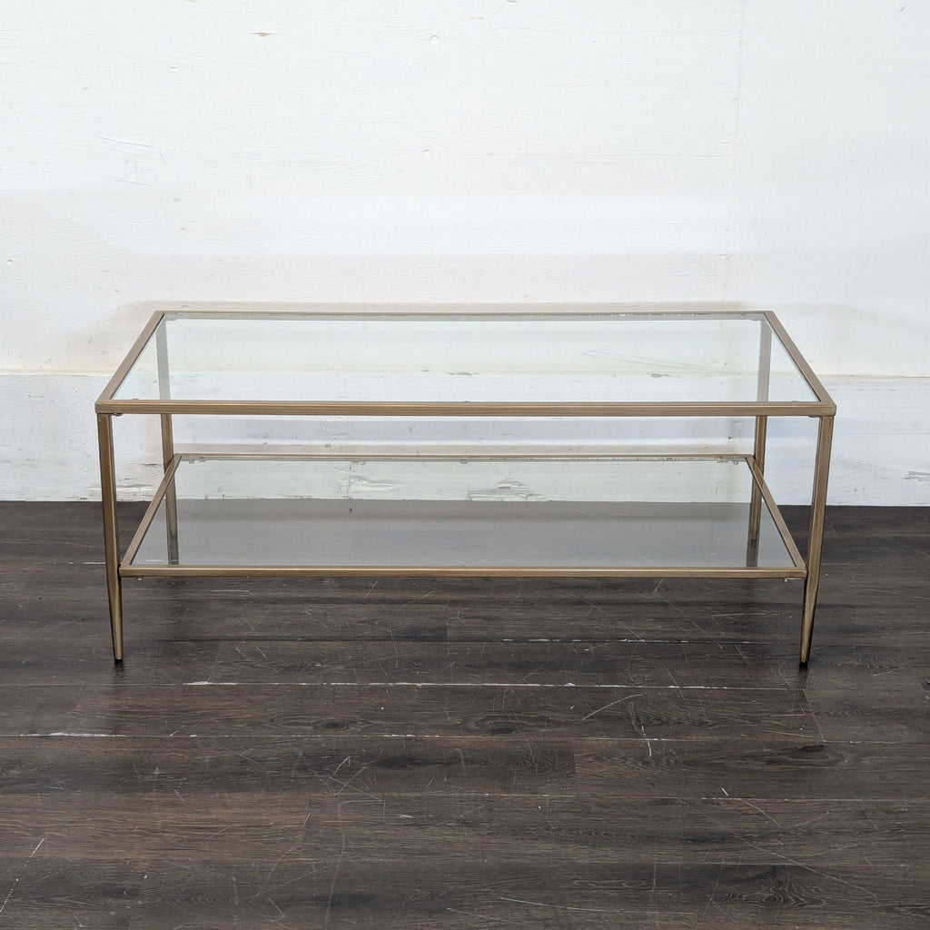 3. Modern glass coffee table with a gold frame, presented against a plain wall on a wooden floor.
