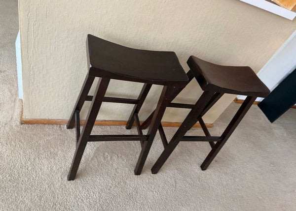 Pair of dark wood Pottery Barn bar stools with contoured seats, placed against a beige wall on carpet.  