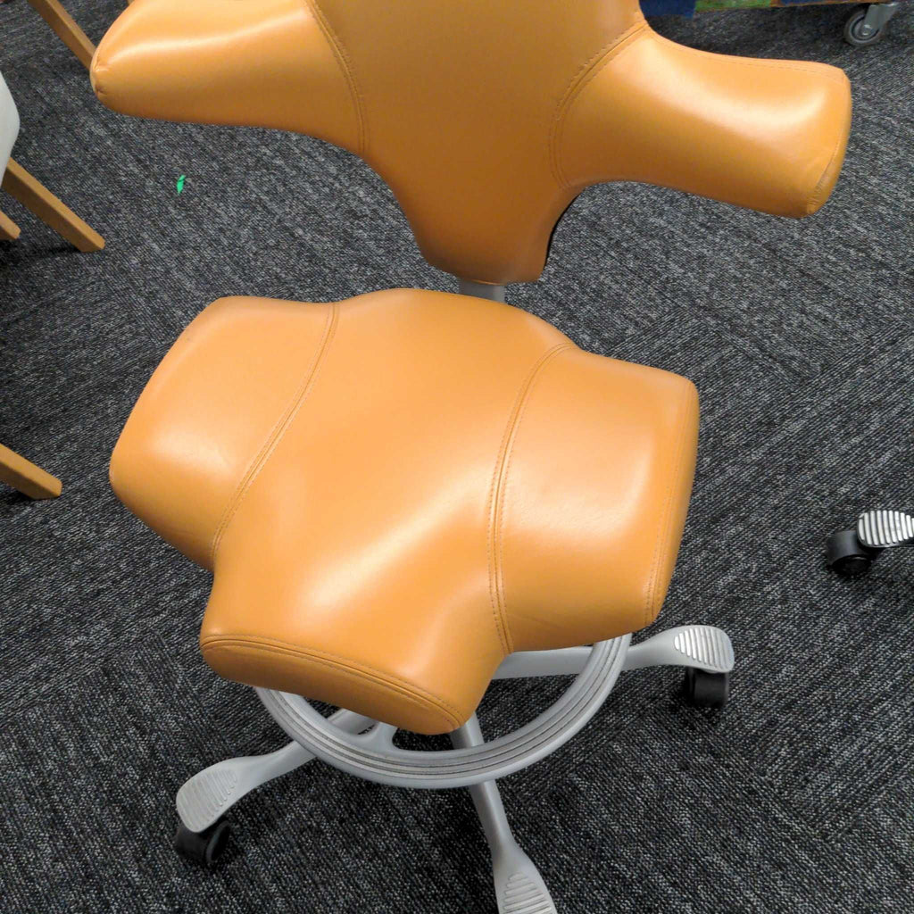 1. Tan HÅG chair with ergonomic saddle-shaped seat and unique winged backrest, shown from above on carpet.