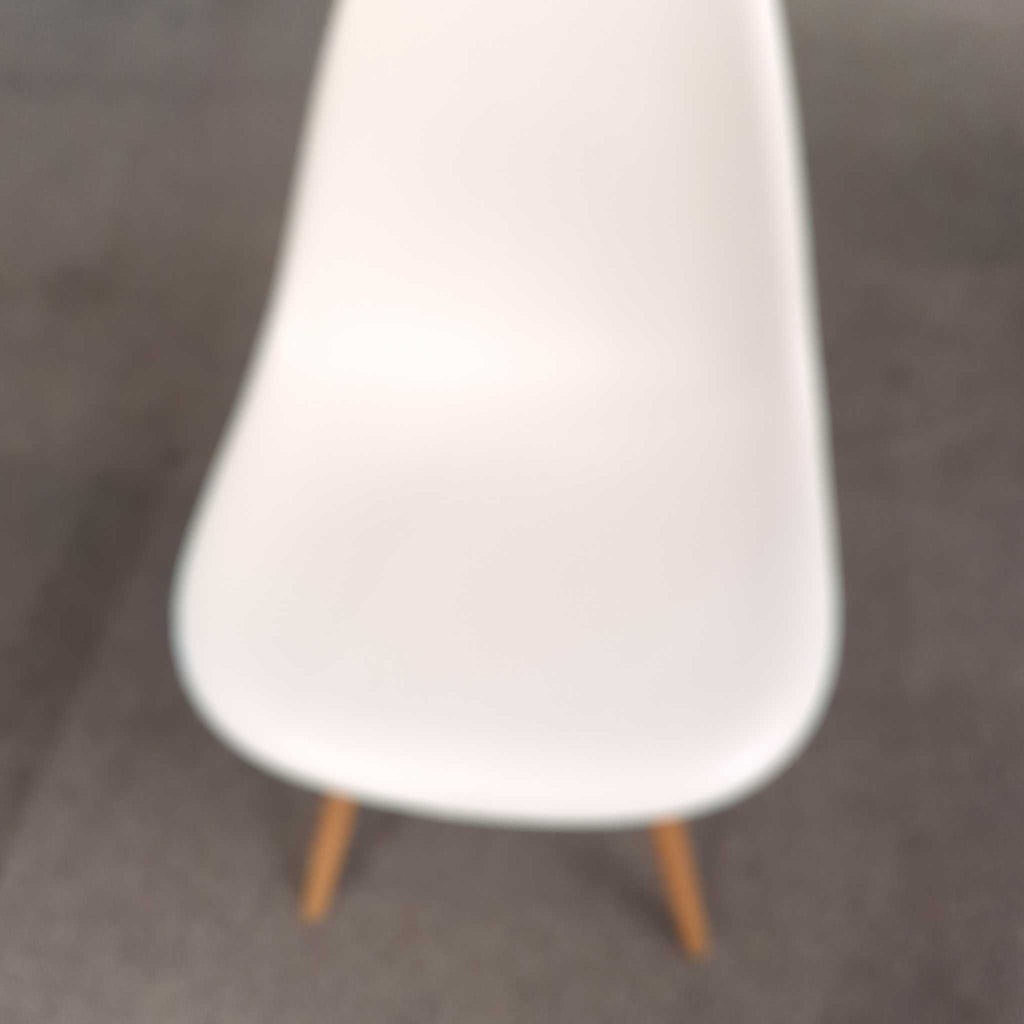 A close-up, slightly blurry image of a white dining chair with wooden legs on a carpeted floor.